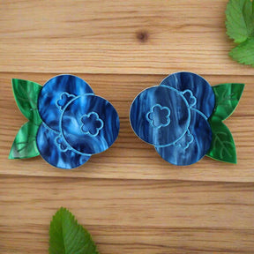 A pair of marbled acrylic blueberry studs with green leaves on a grey background