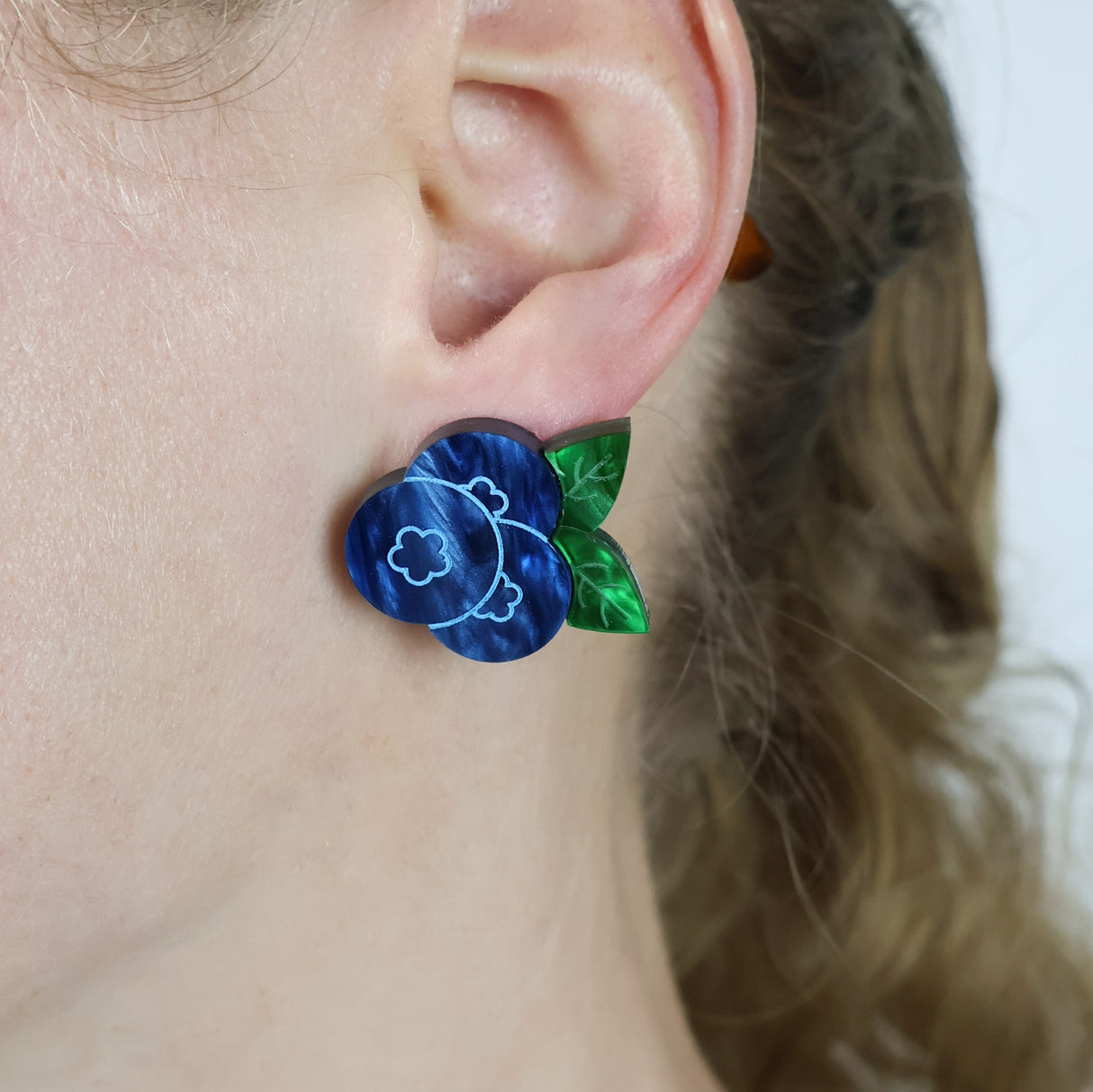 Close-up of an ear wearing blue and green blueberry earring.