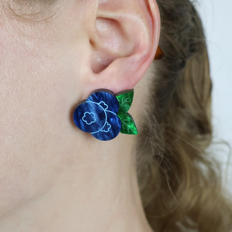 Close-up of an ear wearing blue and green blueberry earring.