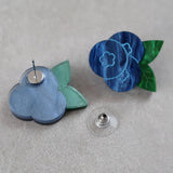 Blue and green blueberry acrylic earrings on a gray surface. One earring is turned to show the stainless steel earring post. 