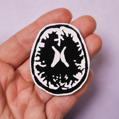 A black and white brooch of a Brain MRI being held in a hand