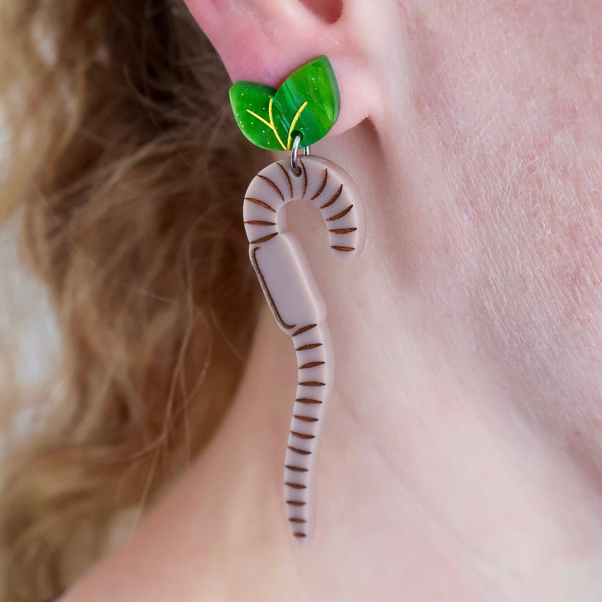 Earring with green leaf topper and brown striped worm dangle design worn on an ear