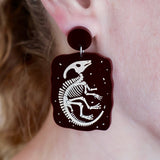 Brown Dinosaur skeleton earring on a person's ear