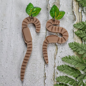 Brown Earthworm-shaped asymmetrical earrings with green leaf toppers. Science inspired laser cut acrylic earrings for biology lovers. 