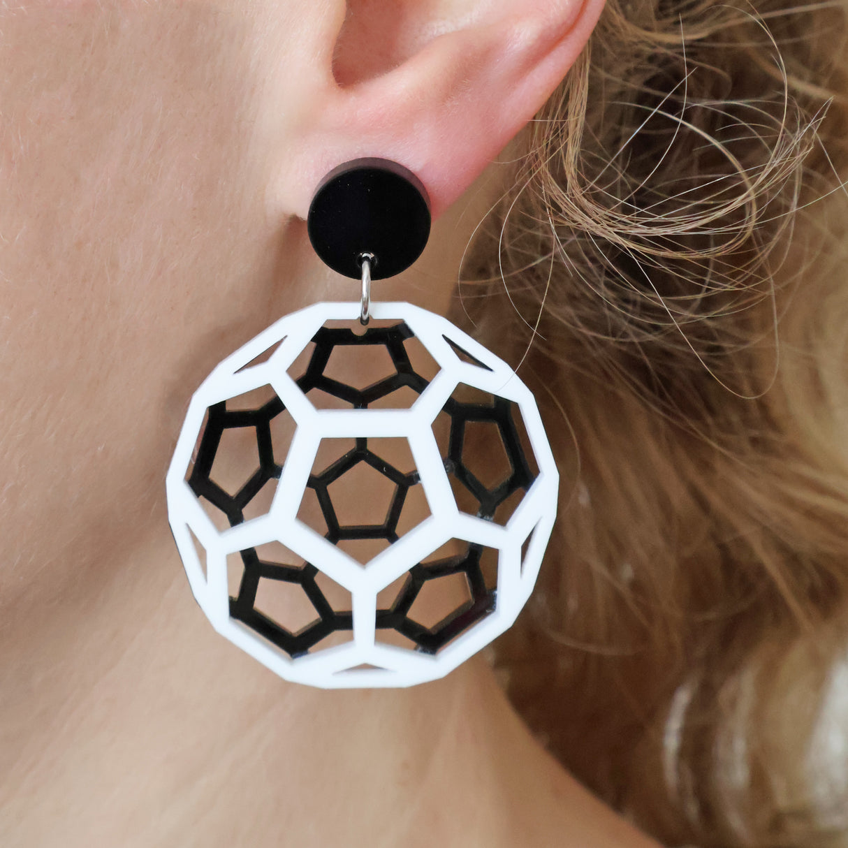 Geometric black and white acrylic earrings worn depicting a bucky ball worn by a person with blonde hair.
