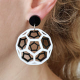 Geometric black and white acrylic earrings worn depicting a bucky ball worn by a person with blonde hair.