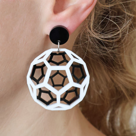 Geometric black and white acrylic earrings worn depicting a bucky ball worn by a person with blonde hair.