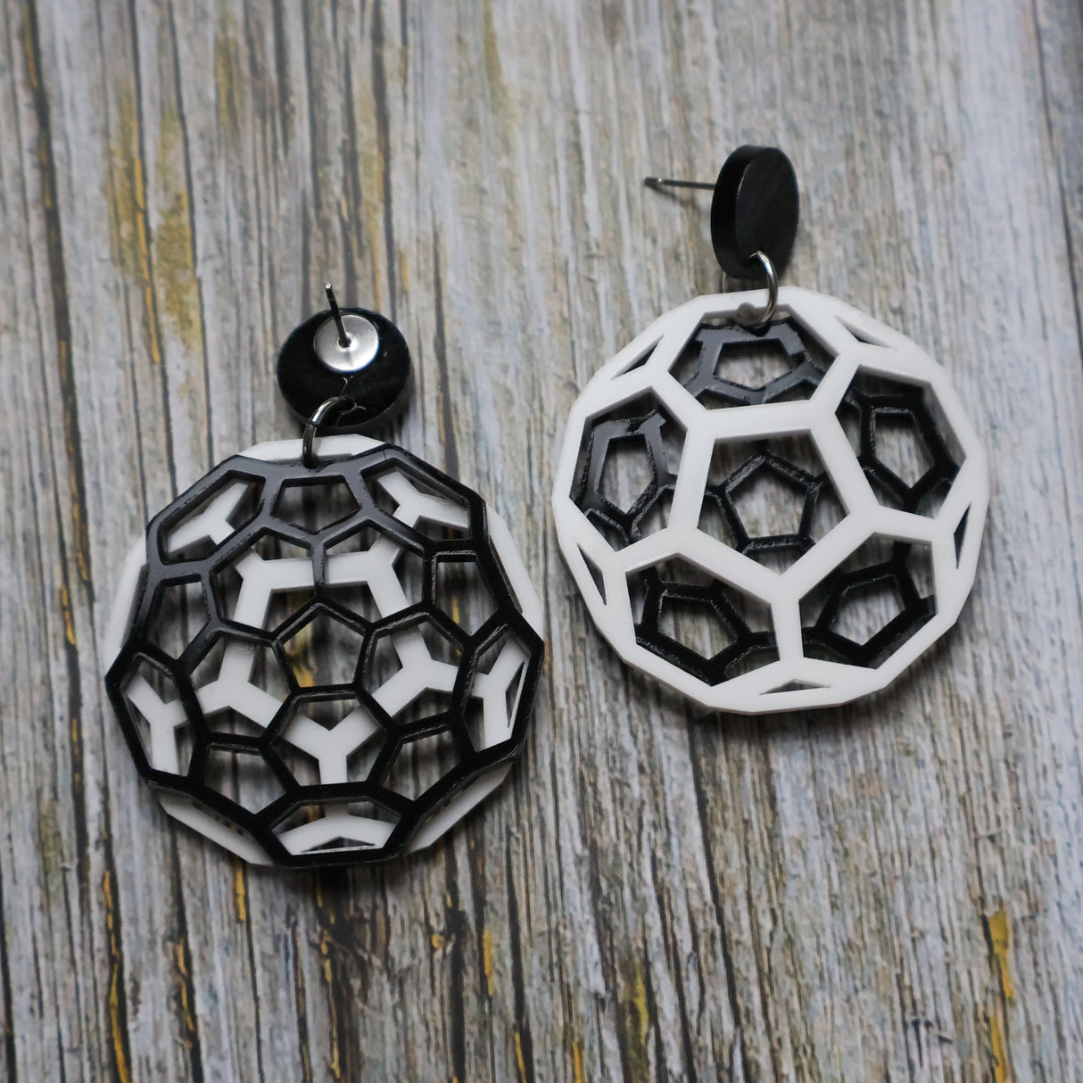 Geometric black and white earrings shaped like carbon bucky balls on a wooden surface. One earring is turned to show the back.