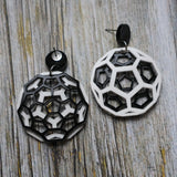 Geometric black and white earrings shaped like carbon bucky balls on a wooden surface. One earring is turned to show the back.