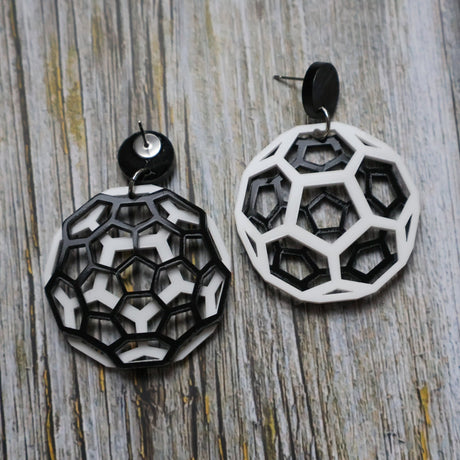 Geometric black and white earrings shaped like carbon bucky balls on a wooden surface. One earring is turned to show the back.