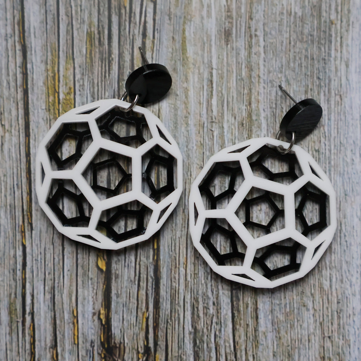 Geometric black and white earrings shaped like carbon bucky balls on a wooden surface