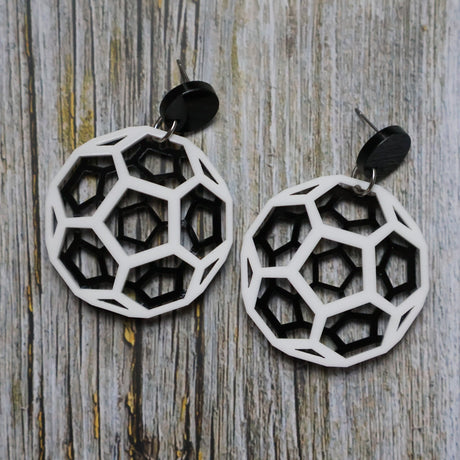 Geometric black and white earrings shaped like carbon bucky balls on a wooden surface