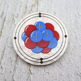Round carbon atom brooch made from laser cut acrylic, showing protons, neutrons and electrons.