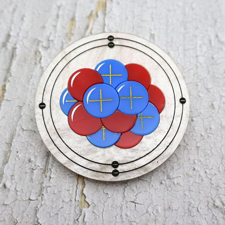 Round carbon atom brooch made from laser cut acrylic, showing protons, neutrons and electrons.