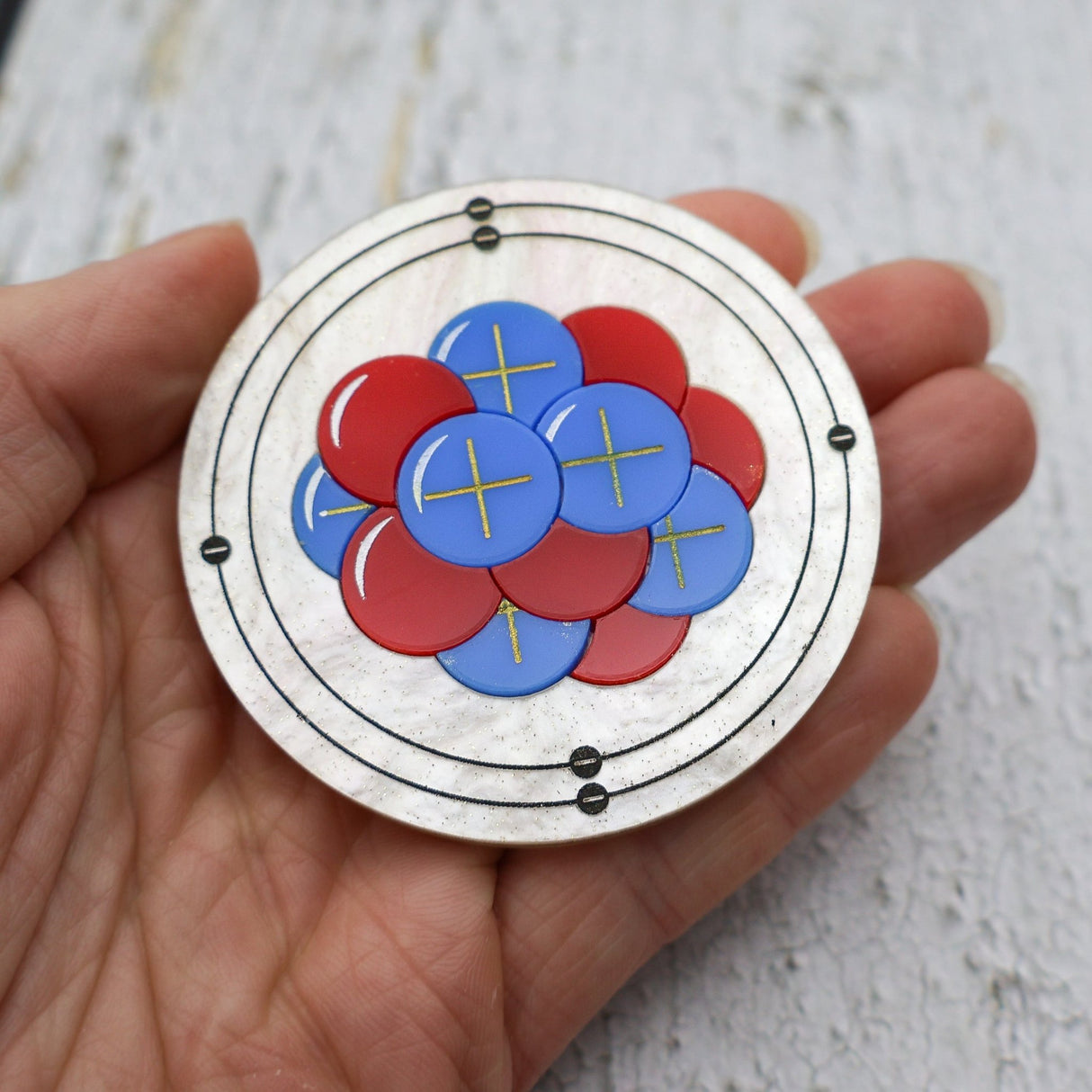 Round carbon atom brooch made from laser cut acrylic. Red and blue Neutrons and Protons form a nucleus within an ivory acrylic body with etched electron orbitals surrounding. 