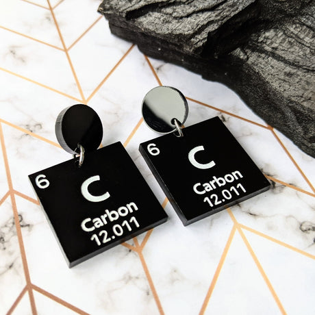 Carbon periodic table earrings, featuring white text on black acrylic squares, which hang from black acrylic round toppers.