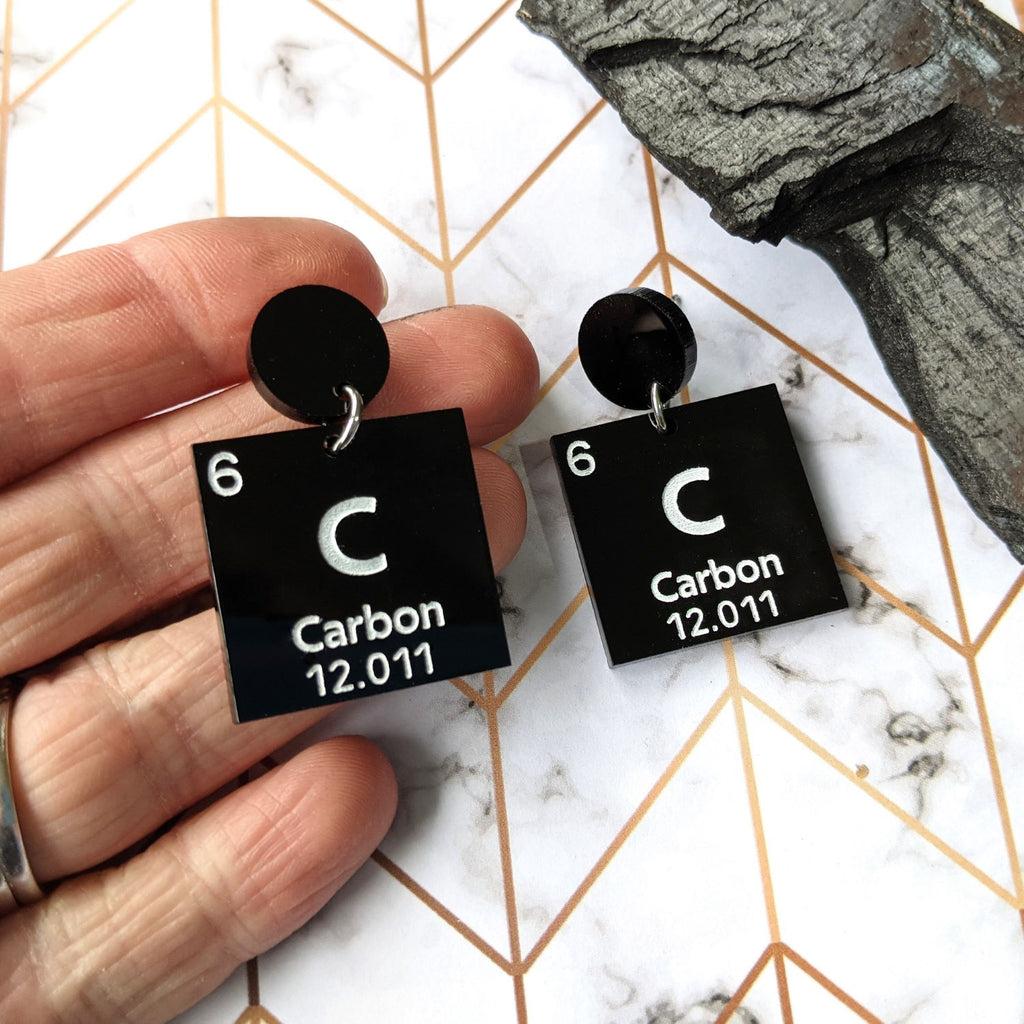 Carbon periodic table earrings, featuring white text on black acrylic squares, which hang from black acrylic round toppers.