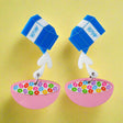 Pair of acrylic earrings shaped like a milk carton pouring into a bowl of cereal on a gray background