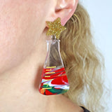 Conical Flask shaped acrylic earrings apoearing to be filled with Christmas colours and a star-shaped gold glitter top being modelled on an ear