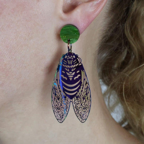 Dangle Earrings with cicada design and green acrylic toppers worn on a person's ear
