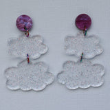 Pair of clear glittery cloud-shaped earrings with purple circular tops on a light gray background.
