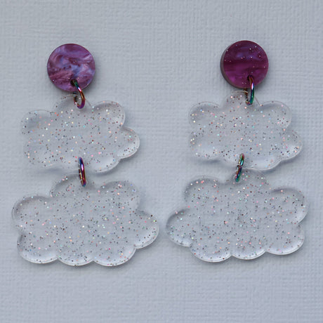 Pair of clear glittery cloud-shaped earrings with purple circular tops on a light gray background.