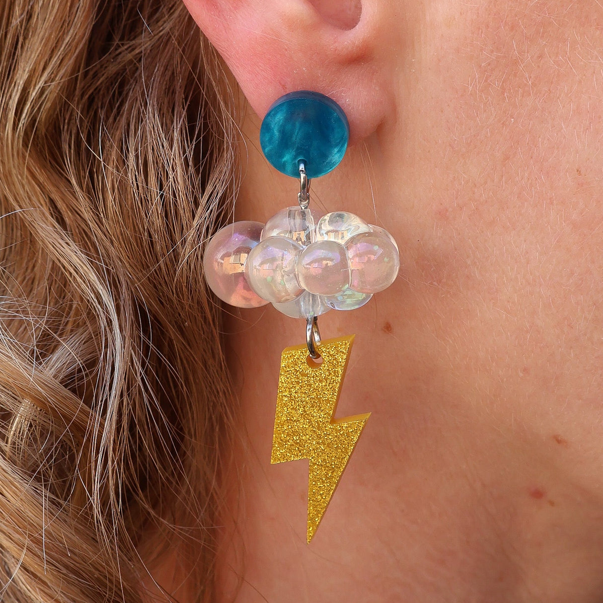 Close-up of a person wearing a colorful earring with an iridescent floud bead and gold lightning bolt charm.