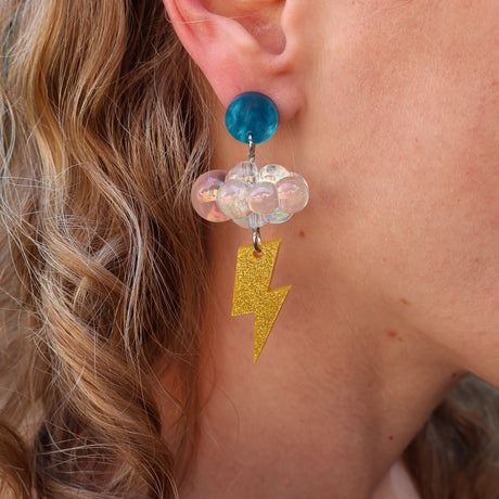 Close-up of a person wearing a colorful earring with an iridescent floud bead and gold lightning bolt charm.