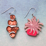 An asymmetrical pair of acrylic earrings with an orange clownfish n one side and a pink sea anemone on the other. Topped with stainless steel french hooks. 