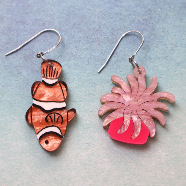An asymmetrical pair of acrylic earrings with an orange clownfish n one side and a pink sea anemone on the other. Topped with stainless steel french hooks. 
