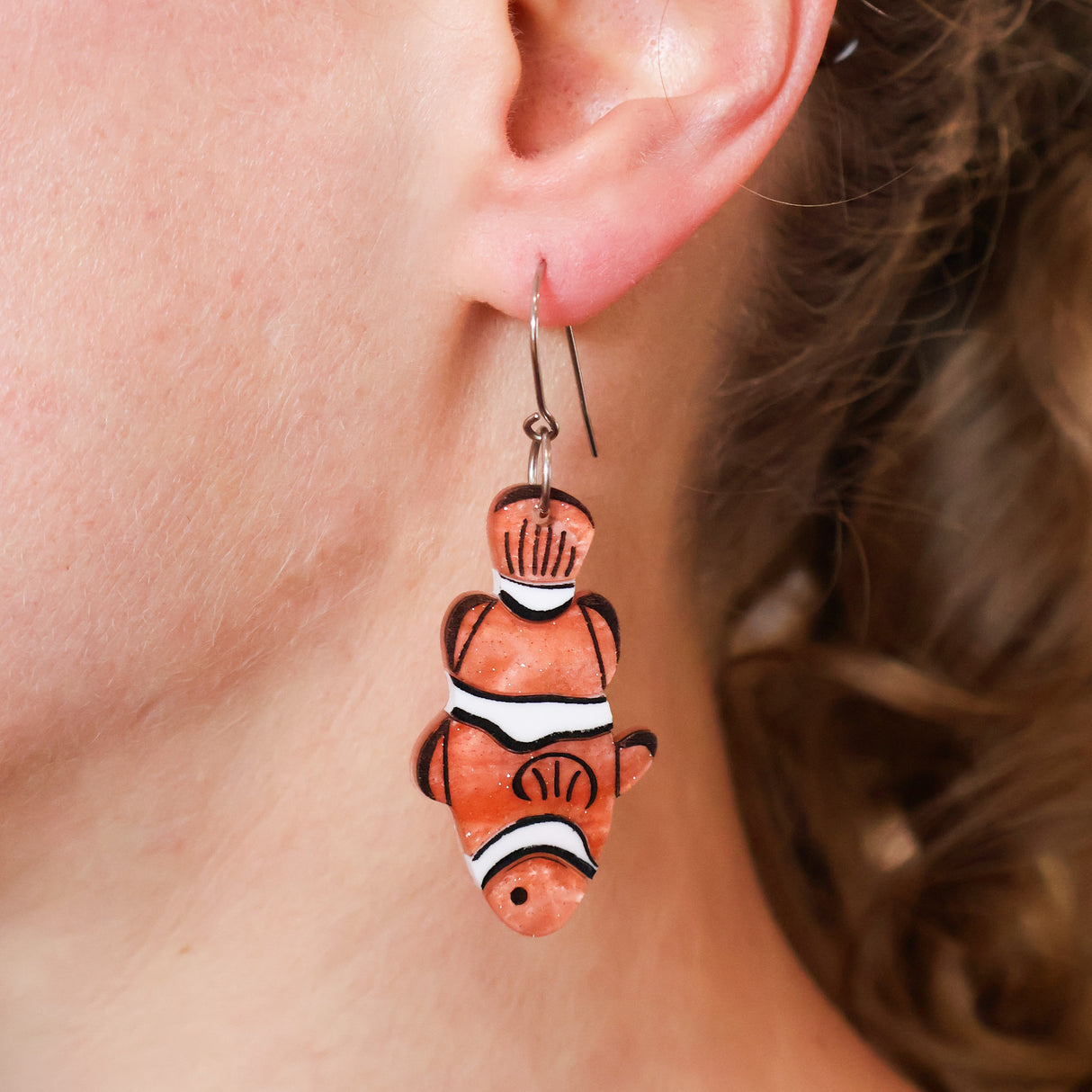 Close-up of a person wearing clownfish-shaped earrings.