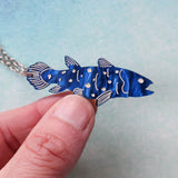 Blue fish-shaped pendant held by a hand against a light blue background