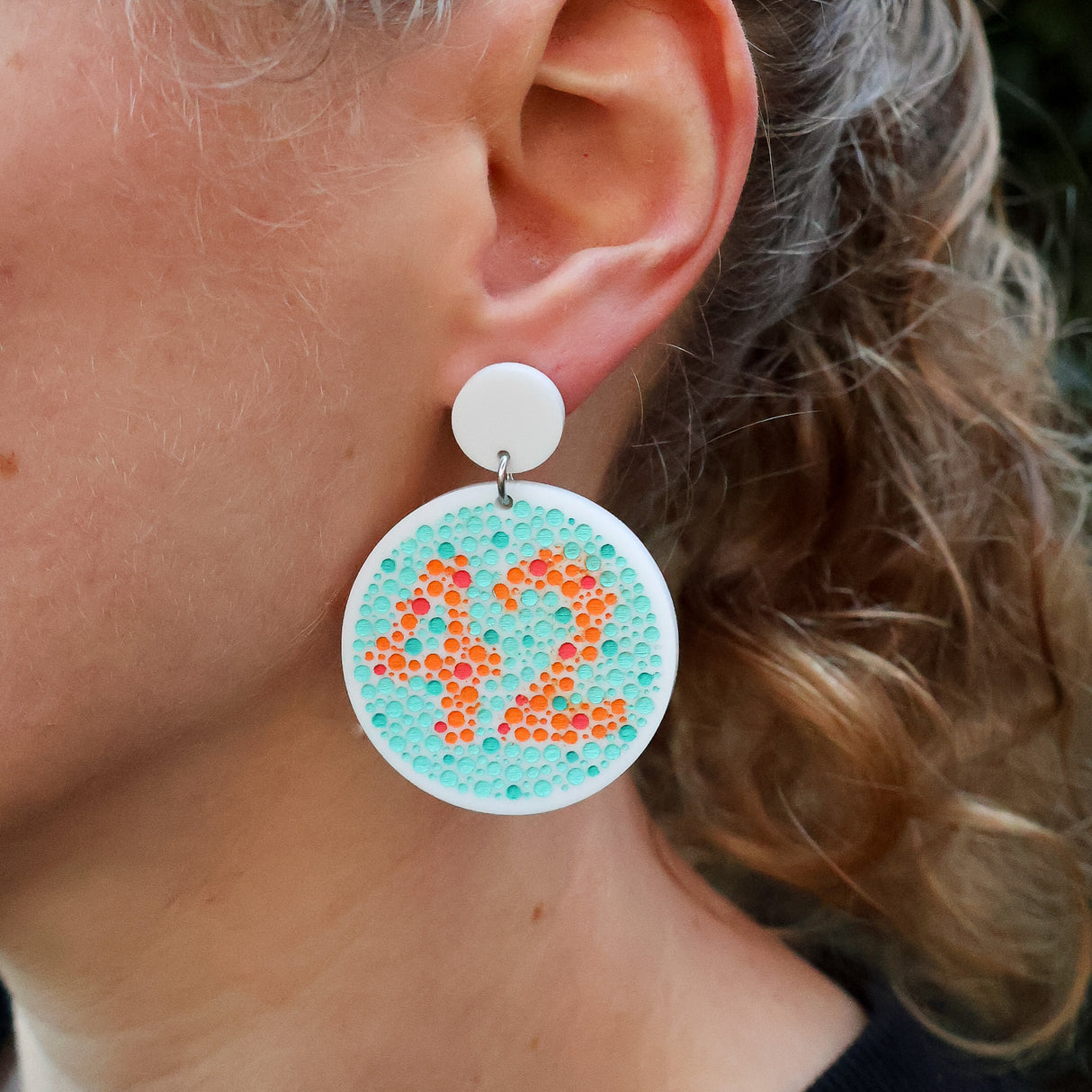 Close-up of a person wearing a colourful colourblindness test earring with the number 42.