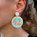 Close-up of a person wearing a colourful colourblindness test earring with the number 42.