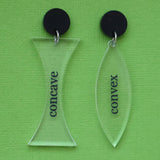 A pair of acrylic earrings labeled 'concave' and 'convex' on a green background, with black acrylic toppers. 