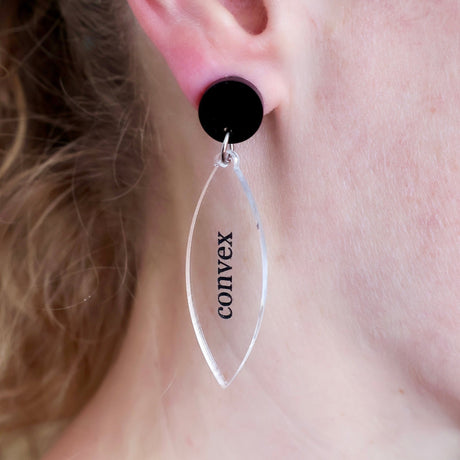Clear lens shaped acrylic earring with 'convex' text and a black round topper modelled on an ear