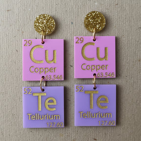 Pair of earrings with periodic table elements spelling CuTe in purple, pink and gold tones. 