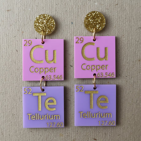 Pair of earrings with periodic table elements spelling CuTe in purple, pink and gold tones. 