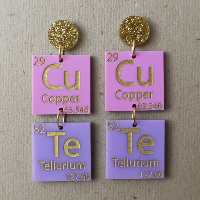 Pair of earrings with periodic table elements spelling CuTe in purple, pink and gold tones. 