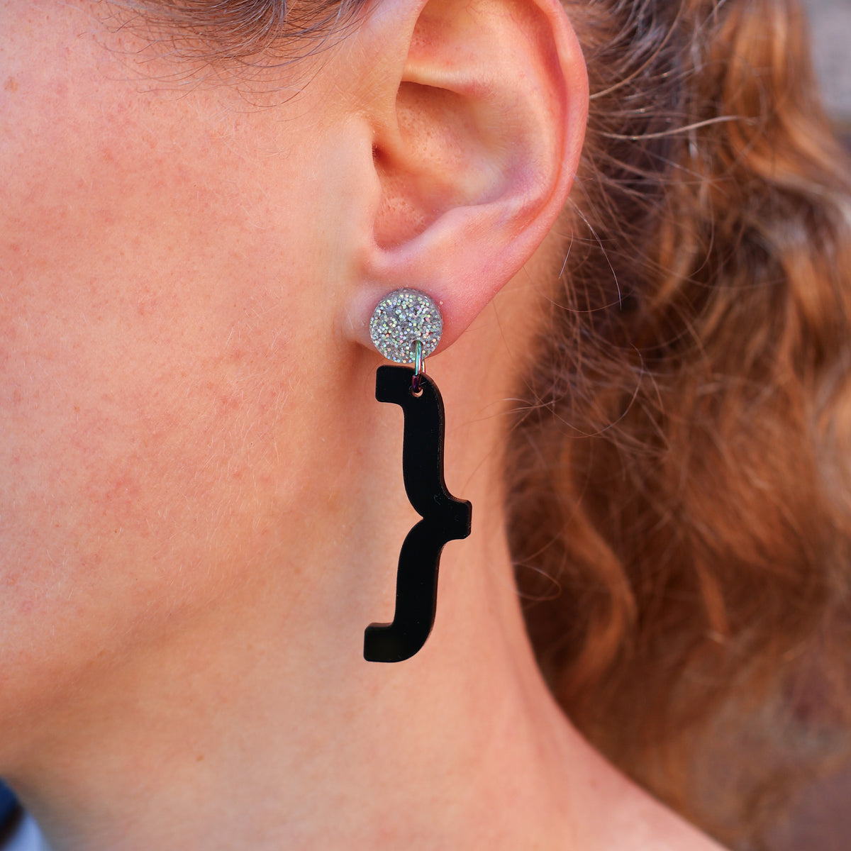 A woman modelling a pair of curly bracket acrylic earrings. 