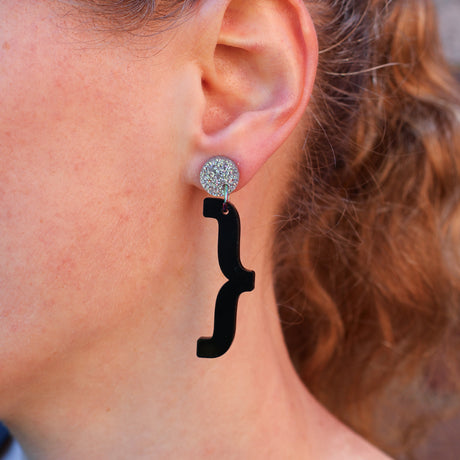 A woman modelling a pair of curly bracket acrylic earrings. 