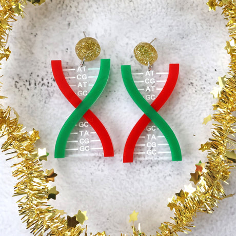 Acrylic DNA strand earrings  in red green and gold tones, on a textured white surface with gold tinsel around them