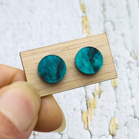 A pair of small swirly green acrylic studs on a wooden backing card.