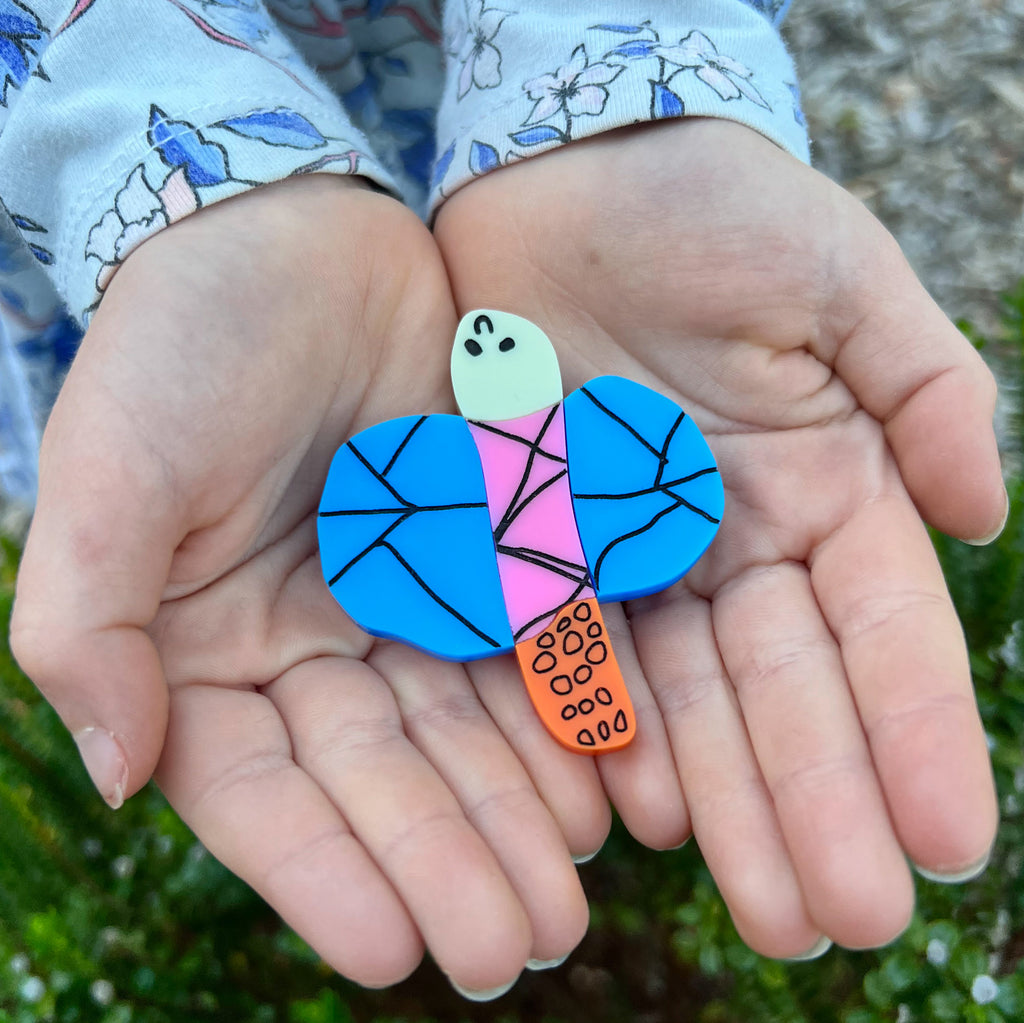 An acrylic dragonfly brooch in the style of a small child's drawing, being held in a small child's hands. Laser cut from acrylic. 