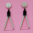 A pair of acrylic earrings shaped like a set of drawing compasses.