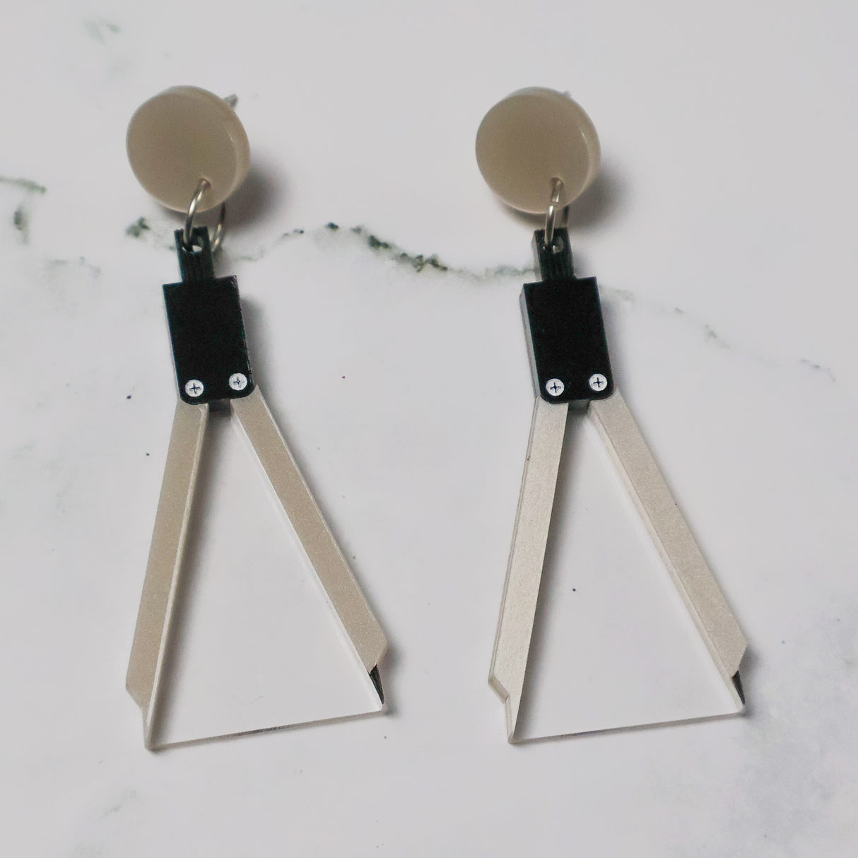 A pair of acrylic earrings shaped like a set of drawing compasses.
