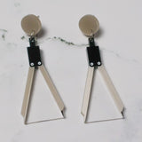 A pair of acrylic earrings shaped like a set of drawing compasses.