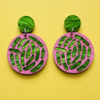 A pair of acrylic earrings with pink and green tones, showing an ecoli colony up close. 