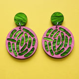 A pair of acrylic earrings with pink and green tones, showing an ecoli colony up close. 