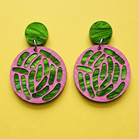 A pair of acrylic earrings with pink and green tones, showing an ecoli colony up close. 